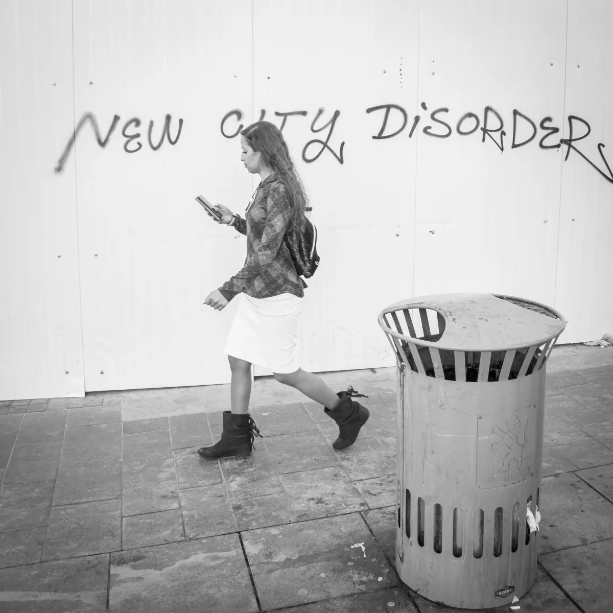 Woman walking past NEW CITY DISORDERS graffiti while looking at her phone